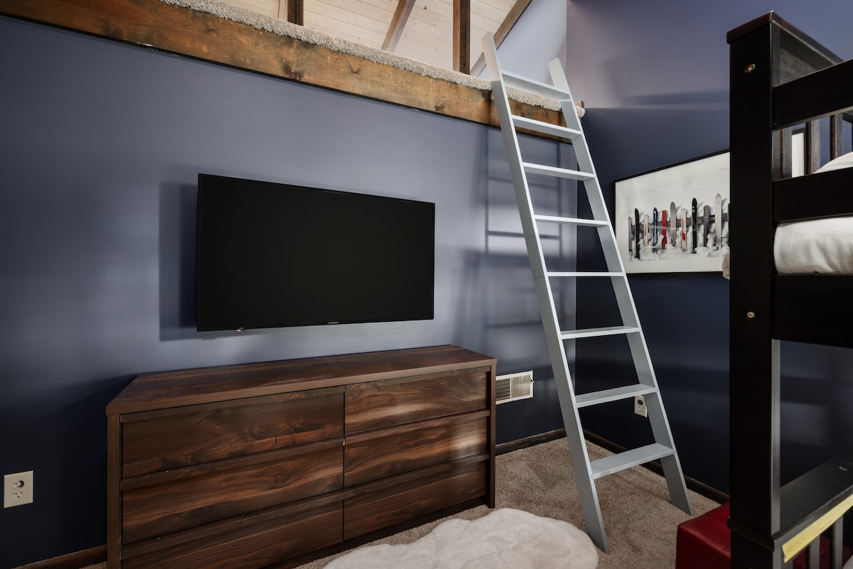 Bunk room with a TV and ladder leading toward the kids’ loft